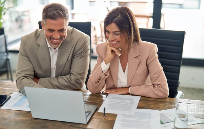 two people smiling while looking at a laptop