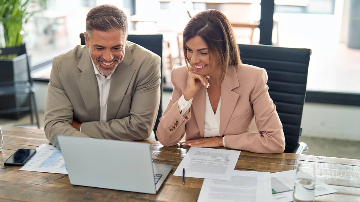 two people smiling while looking at a laptop